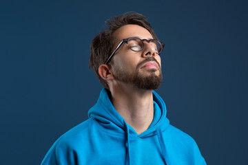 Serene young man wearing glasses closing his eyes in peaceful pose