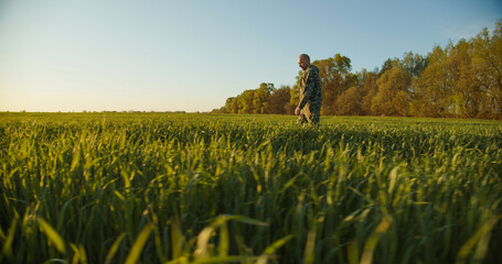 Farmer walks through a young green field during sunset. Adult man farmer walking and checks  his agriculture field. Human walking on agriculture field.   Person walks on high green grass - 755885038