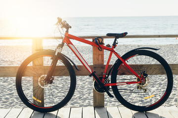 Red bicycle leaning on a wooden fence at the beach during sunset with sand and ocean in the background