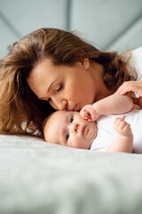 Happy Mother kissing her newborn baby. Closeup portrait of a loose haired loving mother kissing her child. Young mom with a beautiful infant child at home. Mum loves her infant son..