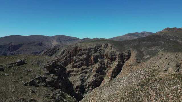 Aerial view - drone flight over a barren mountain landscape towards a gorge - Swartberg Pass, South Africa - cinematic shot