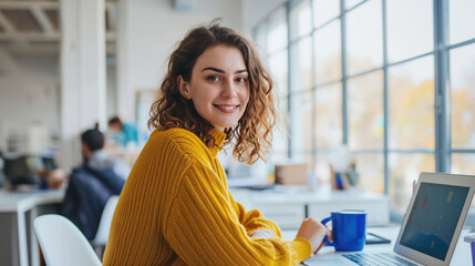Woman smiling while working on a laptop in a bright and modern office environment - obrazy, fototapety, plakaty