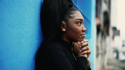 One hopeful young black woman gazing upwards with FAITH and GRATITUDE standing outside in city street. African American adult girl looking UP smiling in urban environment
