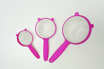 Three pink plastic kitchen strainer. White background.