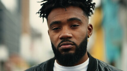 One young black latin man standing outside in urban street looking at camera with serious...
