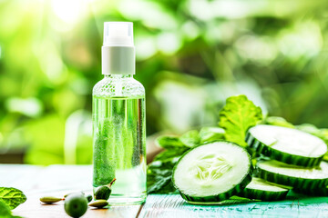 Bottle of cucumber oil sits next to freshly sliced cucumbers on a wooden surface. Organic cosmetics concept. Copy space.