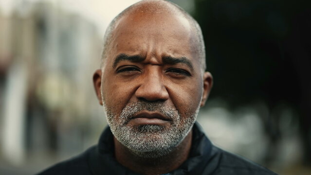 One serious mature black man standing outside in street during drizzle rain looking at camera with concerned expression. Middle-aged 50s person of African descent