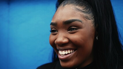 One young black hispanic woman smiling on blue wall, close-up face of a 20s millennial girl of...