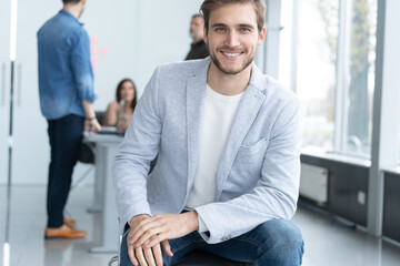 Young confident entrepreneur sitting in modern office smiling and looking at camera