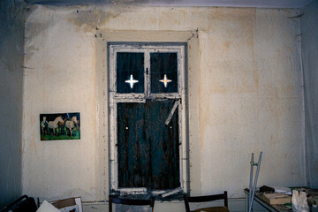 Altes kaputtes Fenster in einem dunklen, chaotisch eingerichtetem Raum, durch das etwas Tageslicht hineinscheint