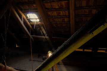 Ein Sonnenstrahl fällt durch ein kleines Dachfenster auf einem alten Dachboden und erhellt den umherfliegenden Staub