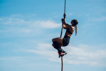 Strong woman climbing a rope while participating in an obstacle course race
