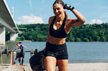 Woman carrying a car tire and looking into the camera during a OCR race