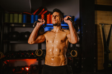 Fototapeta na wymiar A masculine strong sportsman is practicing with kettlebells at the gym