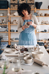 Talented pottery craftswoman standing at studio with earthenware in hands