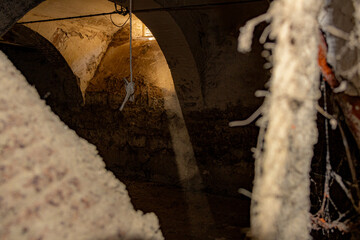 Ein Sonnenstrahl fällt durch ein Fenster in einem alten steinigen Gebäude. Im Vordergrund hängt...
