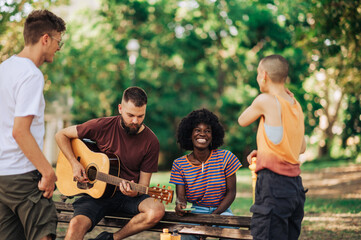 Four multiracial young adults are enjoying their time together and playing guitar.