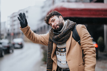 Elegantly dressed young man waving for a cab on a wintery day. He's outdoors, displaying a sense of...