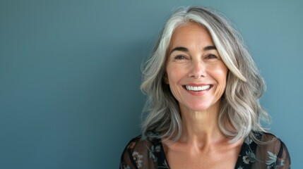 A woman of fifty years old smiles close-up on a blue background. Happy old age, healthy teeth. - obrazy, fototapety, plakaty