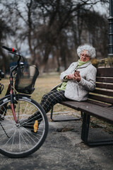 Naklejka premium Mature lady enjoying leisure time in park with bike, engaged with smart phone