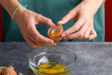 A woman's hand holding the eggshells of breked egg into a clear glass bowl in the gray kitchen table, the process of cooking, fresh eggs into the bowl is ready to cooking, Lifestyle, close up