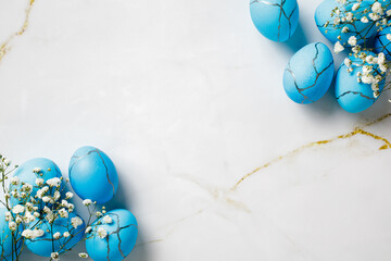 Frame of blue Easter eggs and white flowers on a marble table