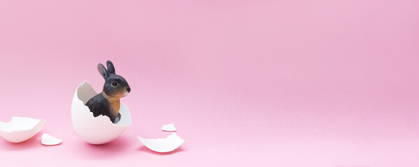 Minimal Easter banner with bunny hatching from an egg on pink background. Creative spring postcard....