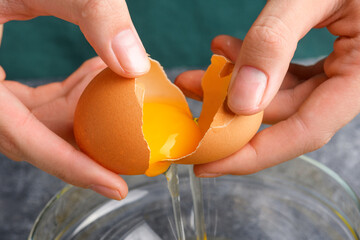 Housewife hands cracking fresh egg, yolk and white dropping in a bowl. A woman's hand cracking an...