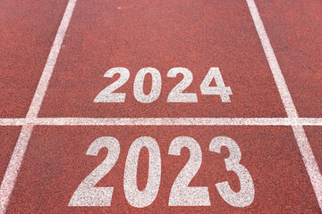 Happy new year 2024 symbolizes the start of the new year. Rear view of a man preparing to run on the athletics track engraved with the year 2024. The goal of Success. Getting ready for the new year.