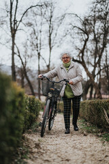 Mature female retiree walking with a bicycle through a peaceful park, embodying an active lifestyle and independence.