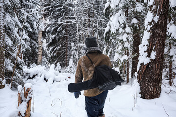 A forester with an ax and a saw walks through a snowy forest, in the foreground there are tree...