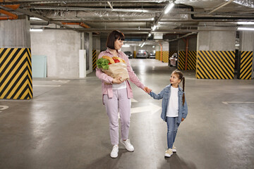 Happy Caucasian young family mother and daughter in casual clothes walking and holding paper bag...