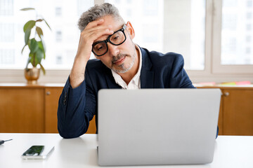 With a hand to his forehead mature businessman seems to be in deep concentration or facing a...