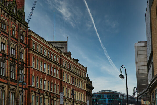 Urban street view with historic buildings under a clear blue sky with contrails in Leeds, UK.