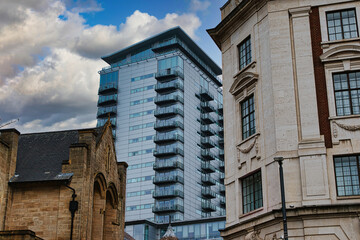 Modern glass skyscraper towering over historic buildings under a cloudy sky in Leeds, UK.