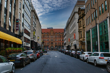 Urban street view with parked cars and historic buildings under a cloudy sky in Leeds, UK.