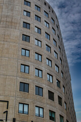 Fototapeta na wymiar Curved modern office building facade with symmetric windows against a cloudy sky in Leeds, UK.