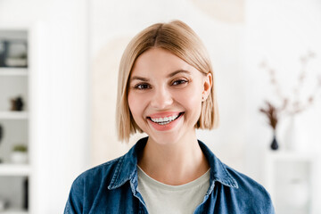 Toothy smile concept. Closeup portrait of blonde young happy girl looking at the camera at home. Caucasian woman in casual clothes cropped photo