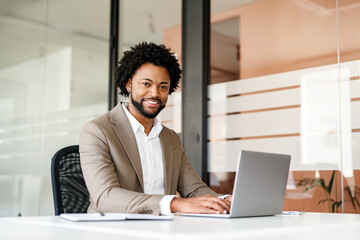 Confident and approachable, an African-American businessman sits at his desk in a modern office, his hands on a laptop keyboard, ready to tackle the day's challenges
