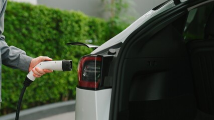 Young man recharge EV electric car in green sustainable city outdoor summer garden as lifestyle of...