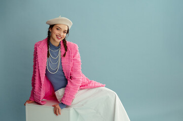 Fashionable happy smiling woman wearing beret, elegant pink tweed blazer, turtleneck, layered pearl necklace, white skirt, posing on blue background. Studio portrait. Copy, empty, blank space for text - 755945802