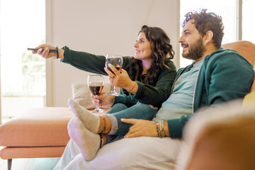 A smiling couple enjoys a television show together during a comfortable evening at home, each...