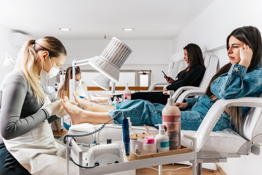 Group of professional podiatrists working in a modern nail beauty studio or spa. Satisfied clients relaxing and enjoying in a great foot and toenails treatment.
