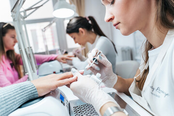 Professional manicurists working in a modern beauty salon. Satisfied female clients receiving nail...