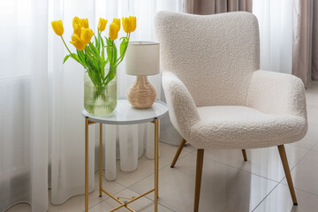 A bouquet of yellow tulips in a vase on the table near the chair. A cozy place to relax at home