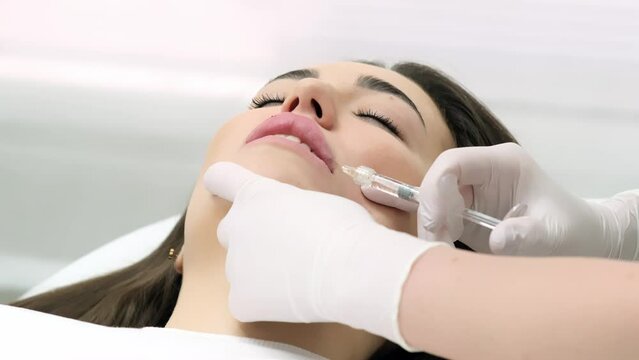 Close-up of a young woman's face undergoing lip augmentation procedure. Cosmetology injections and services. Injection lip correction.