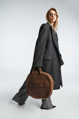 appealing graceful woman with blonde hair in black stylish coat holding brown bag and looking away
