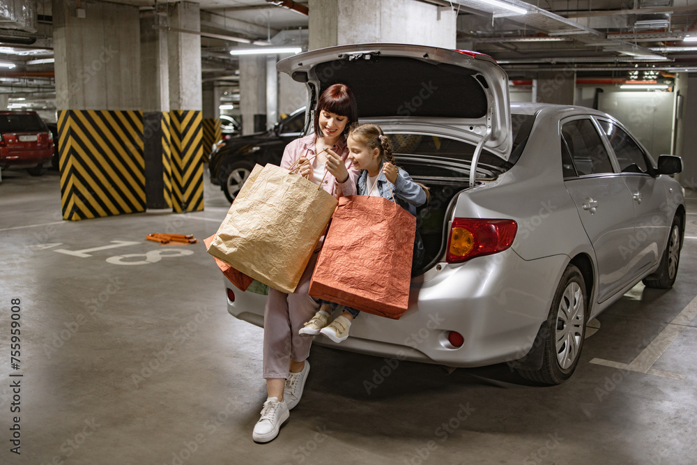 Wall mural dressed in casual attire caucasian family mother and little daughter sitting on open trunk of car in