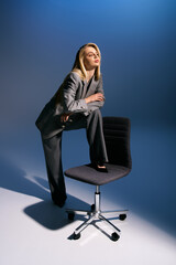 alluring elegant woman with blonde hair in smart silver suit sitting on chair and looking away