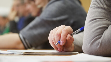 Woman with a fountain pen sits next to her colleagues and prepares to take notes in a notebook during a meeting or training session. An exam or colloquium. Photo. No face